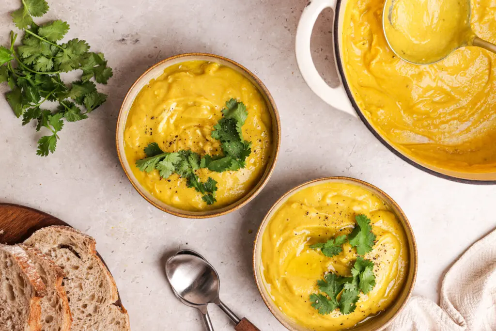 Overhead view of curried parsnip soup served in bowls with coriander and crusty bread