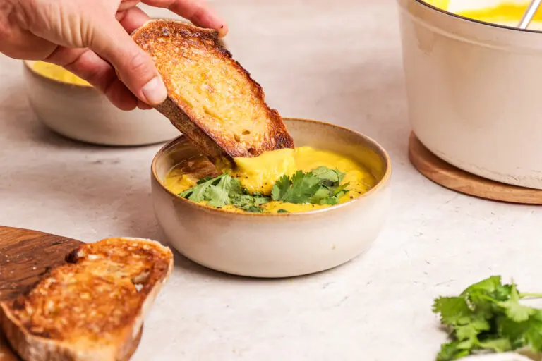 Hand dipping toasted bread into a bowl of creamy curried parsnip soup