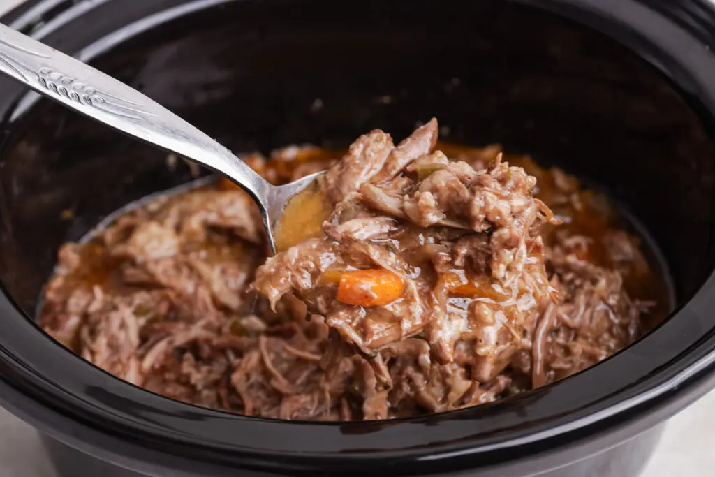 Spoon lifting shredded slow cooker pulled beef coated in thick, rich beef gravy