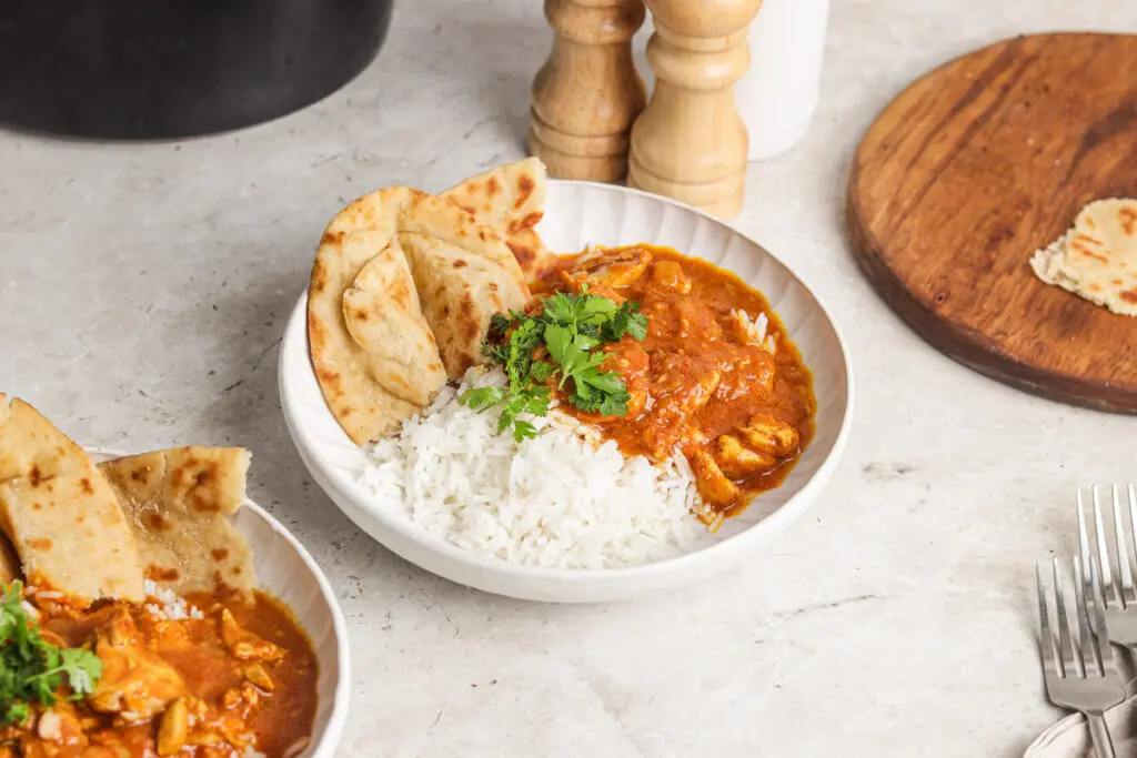 Bowl of slow cooker chicken curry with fluffy rice and naan, coated in rich creamy sauce