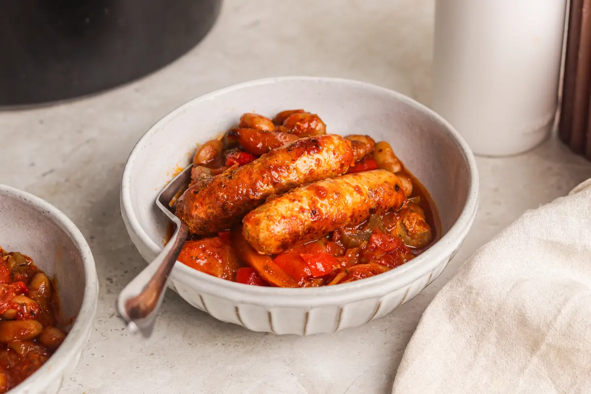 Slow cooker sausage casserole served in a bowl with chicken sausages, vegetables and beans