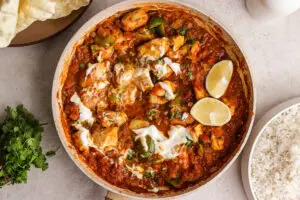Overhead pan of Chicken Bhuna with thick tomato sauce, peppers, tender chicken and yoghurt drizzle