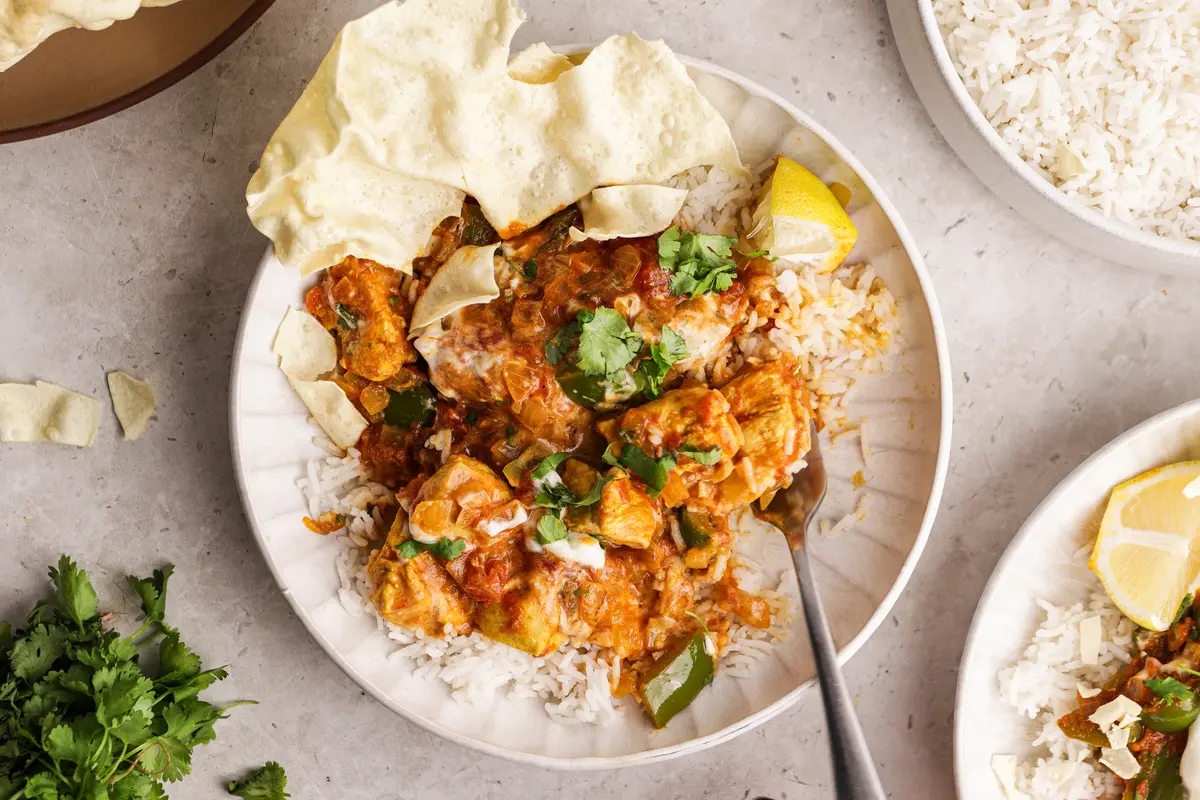 Chicken Bhuna with rice and poppadoms in a bowl, showing chunky chicken and rich sauce.