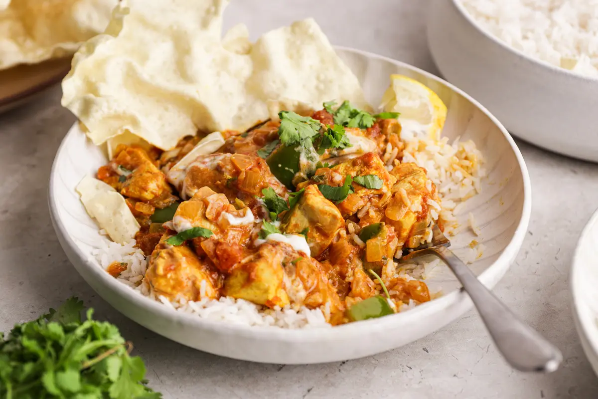 Close-up of Chicken Bhuna on rice with peppers, onions, coriander and creamy yoghurt