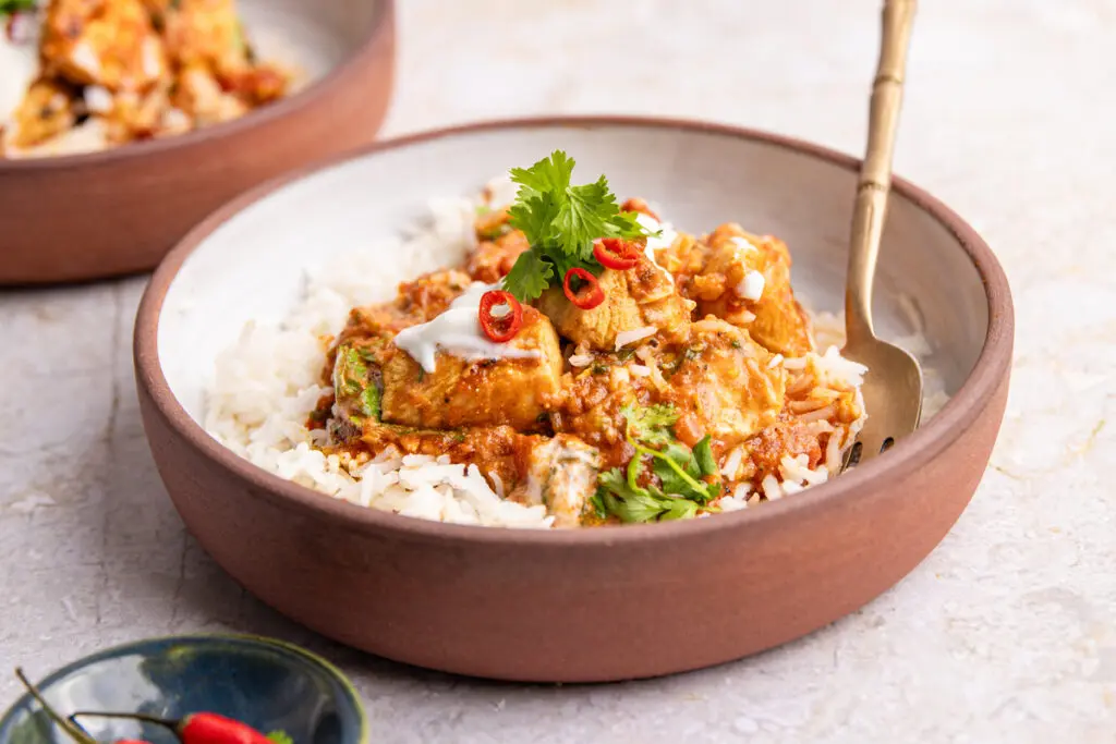 Bowl of healthy Chicken Karahi with rice, topped with yoghurt, coriander and sliced red chilli