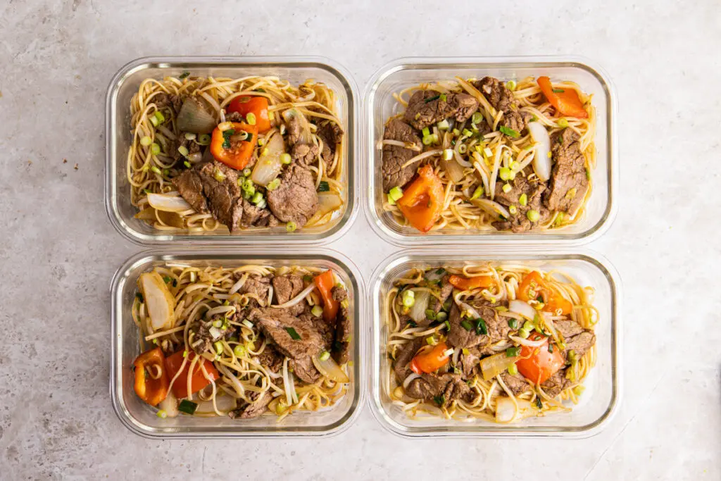 Four glass meal prep containers filled with high-protein Beef Chow Mein viewed from above.