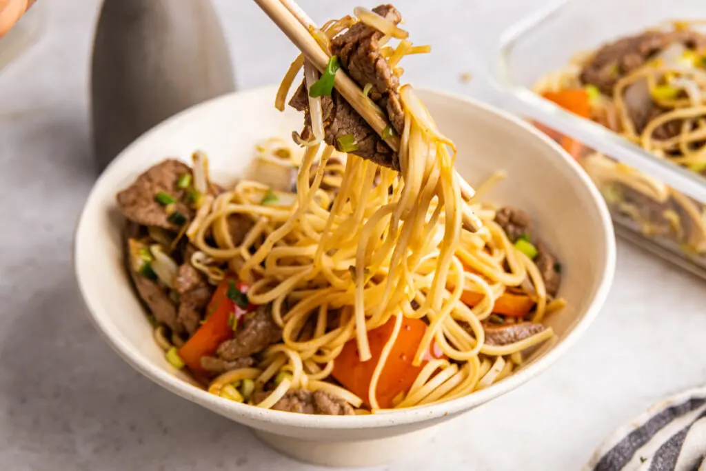 Chopsticks lifting noodles and beef from a bowl of high-protein Beef Chow Mein.