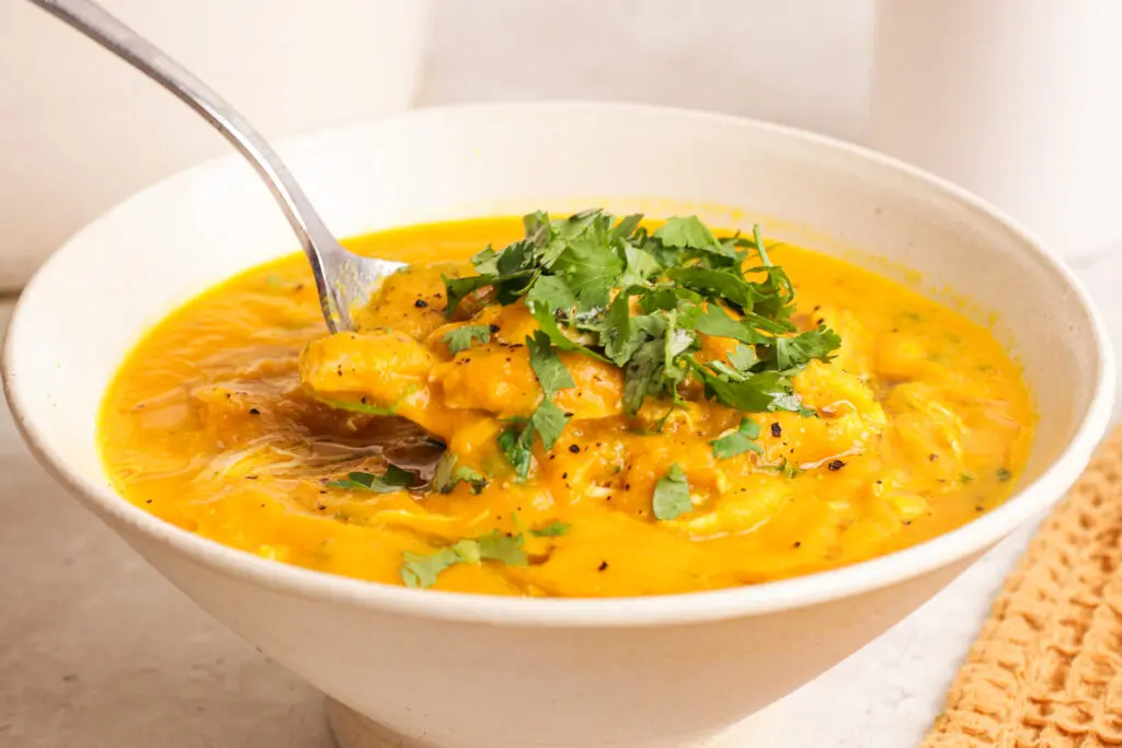 Close-up of carrot and coriander soup with chicken and herbs in a ceramic bowl.