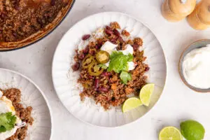 Bowl of chilli con carne on rice with yoghurt, jalapeños, coriander and lime.