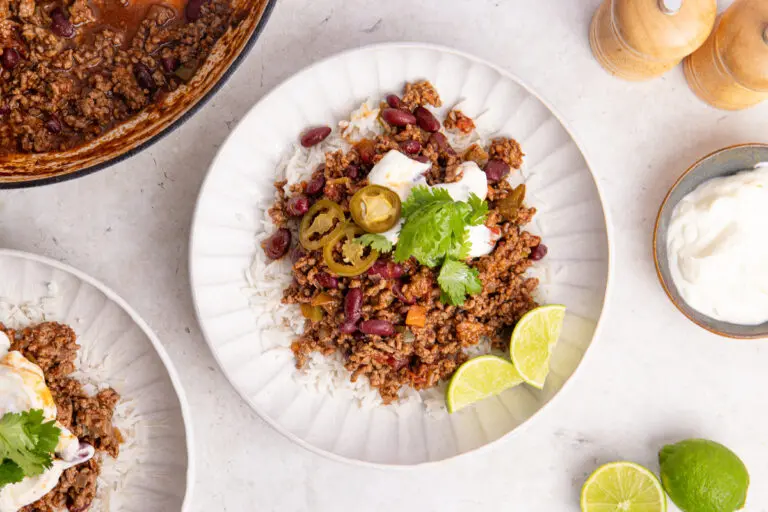 Bowl of chilli con carne on rice with yoghurt, jalapeños, coriander and lime.
