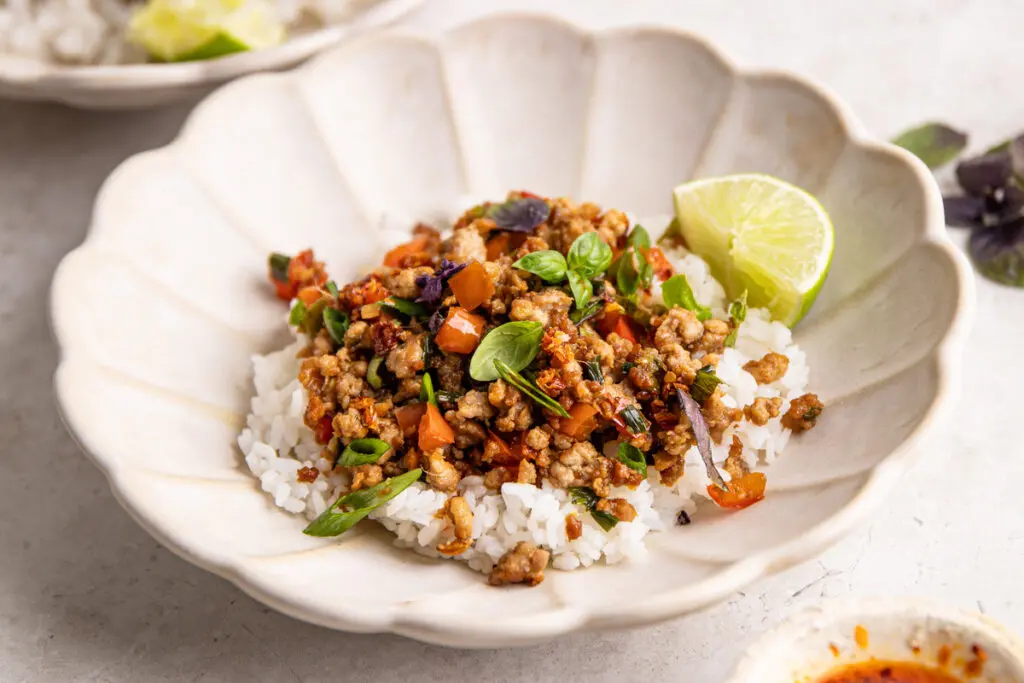 High-protein Thai basil pork mince stir fry on rice with lime and fresh basil leaves