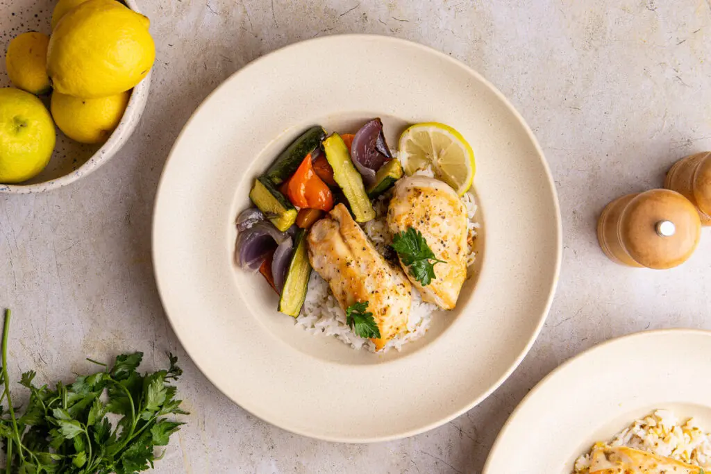 Italian lemon chicken served on rice with roasted vegetables and lemon garnish
