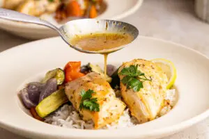 Honey lemon sauce being poured over juicy chicken on rice with vegetables