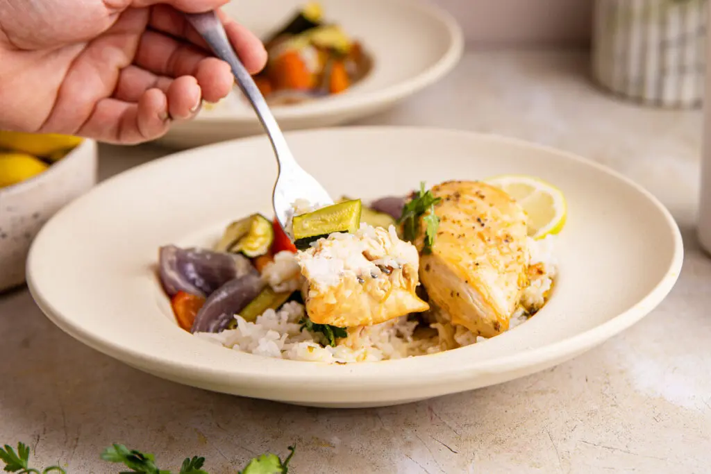 Close-up fork lifting tender lemon chicken with rice and vegetables