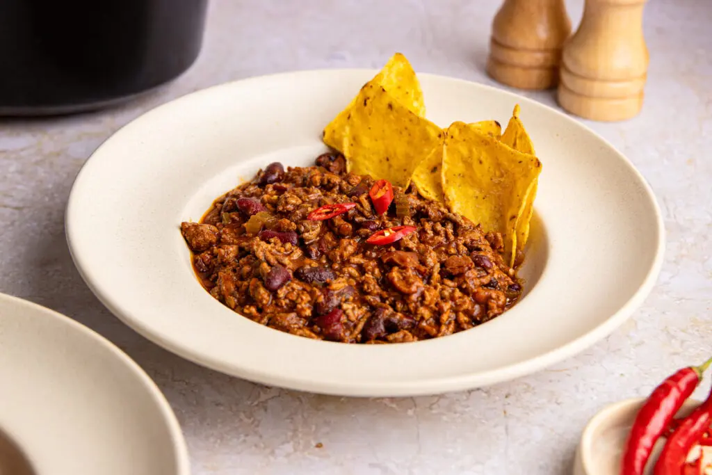 Close-up bowl of slow cooker chilli con carne with tortilla chips garnish