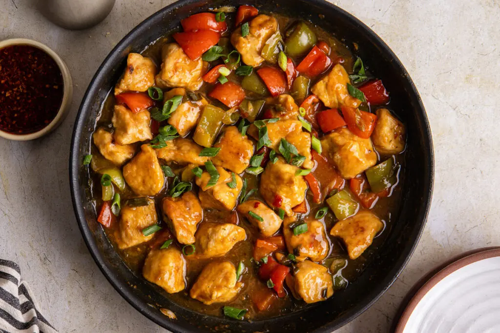 Sticky sweet chilli chicken in wok with peppers and spring onion garnish