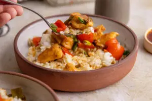 Fork lifting sweet chilli chicken and rice showing sticky sauce coating