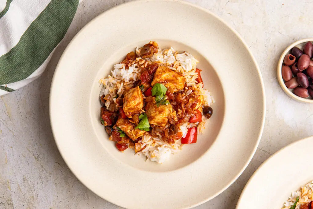 Brazilian chicken stew served over rice with parsley garnish on neutral plate