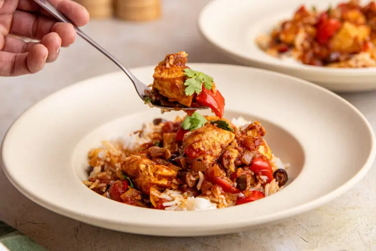 Fork lifting chicken from Brazilian chicken stew over rice with rich tomato sauce