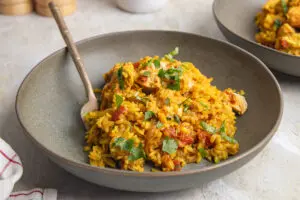 Bowl of chicken pilau with fluffy golden rice, chicken breast and coriander
