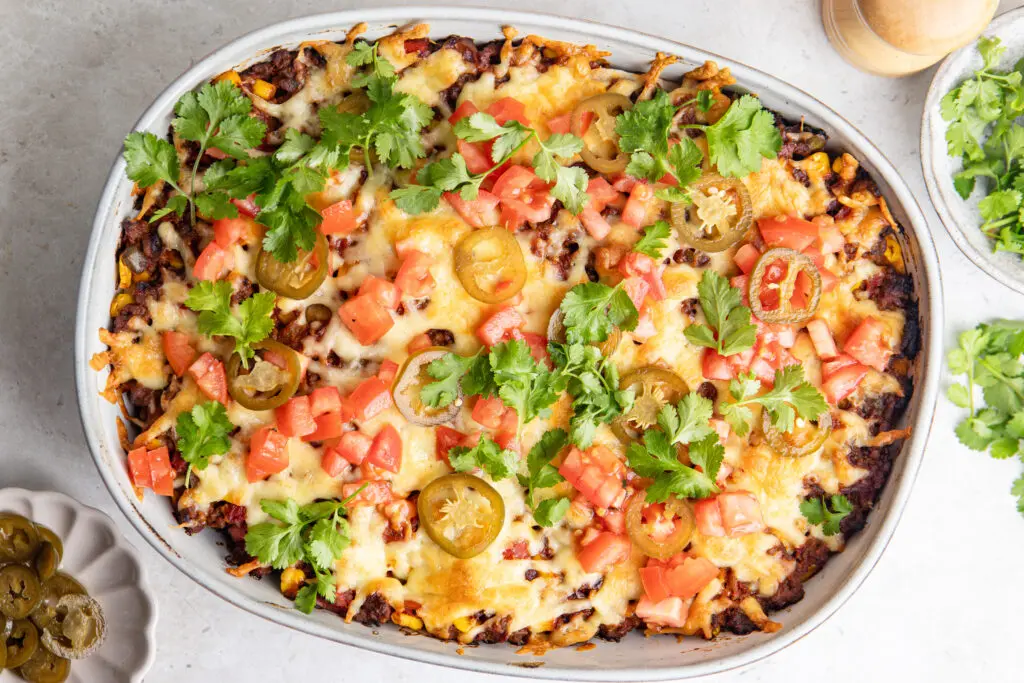 High-protein Mexican lasagne topped with melted cheese, tomato, jalapeños and coriander
