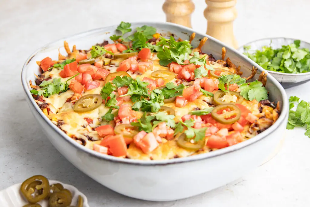 Mexican lasagne in a baking dish with golden cheese, tomato, jalapeños and fresh coriander