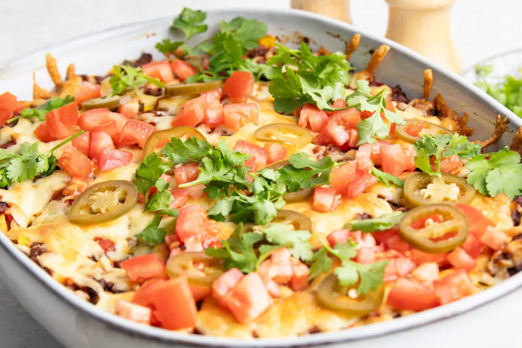 Close-up of cheesy Mexican lasagne topped with diced tomato, jalapeños and coriander