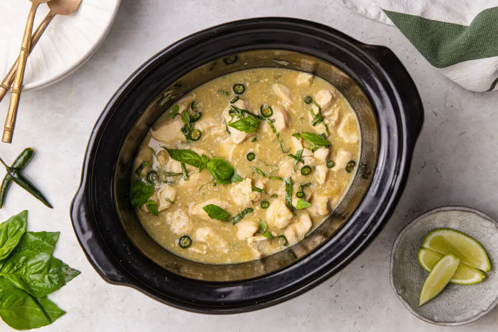 Slow cooker Thai green chicken curry with basil, sliced chilli and lime wedges