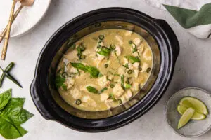 Slow cooker Thai green chicken curry with basil, sliced chilli and lime wedges