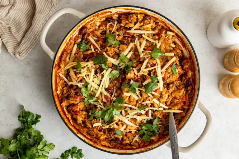 Creamy chilli con carne orzo in a pan topped with cheddar and fresh coriander