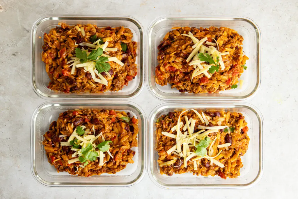 Four meal prep portions of chilli con carne orzo topped with cheddar and coriander