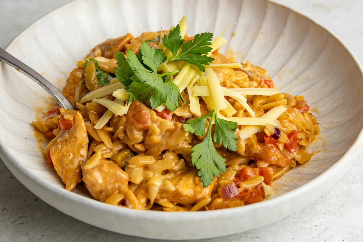 Close-up of creamy BBQ chicken orzo topped with grated cheddar and fresh parsley.