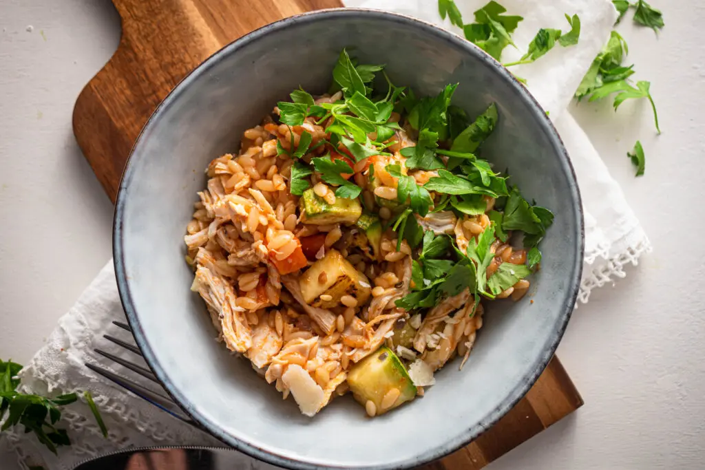 Chicken and orzo casserole with courgette, tomatoes, Parmesan and fresh parsley in a bowl.