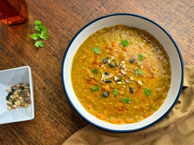 Spiced lentil high protein soup served in a white bowl, topped with seeds and fresh parsley
