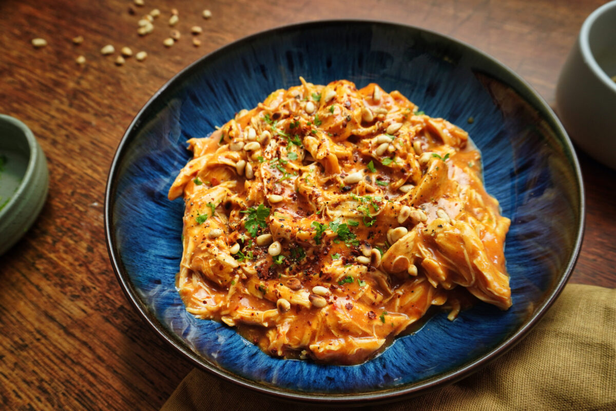 A close-up of tender, shredded harissa chicken glistening in its spicy, smoky sauce.