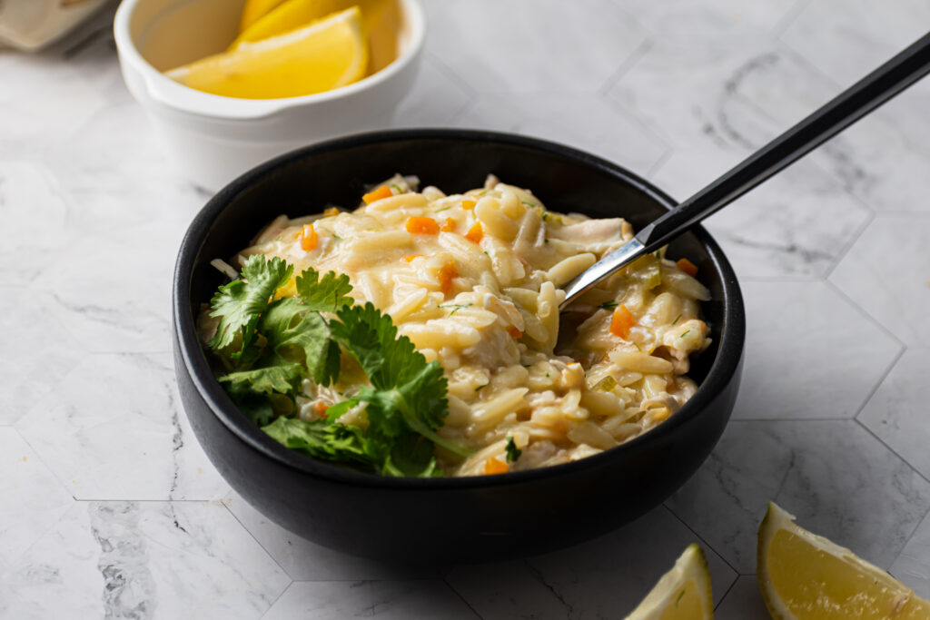 Creamy chicken and orzo soup with vegetables, fresh herbs and lemon wedges.